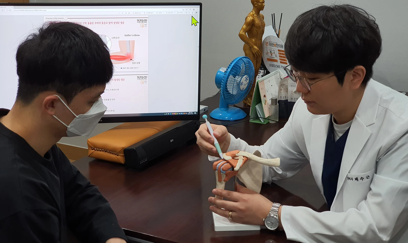 대표원장이 환자에게 어깨 관절 모형을 가리키며 설명하는 모습